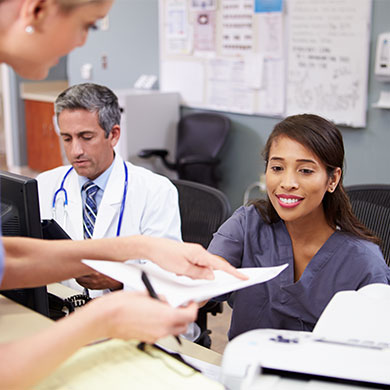 two people in scrubs discuss paperwork over reception desk